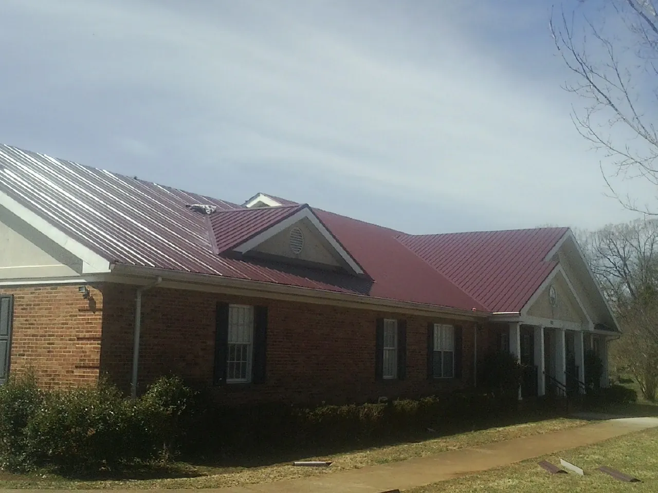 Red metal roof with gabled entries on a long brick building, from a Hail Damage Roof Repair job in Council