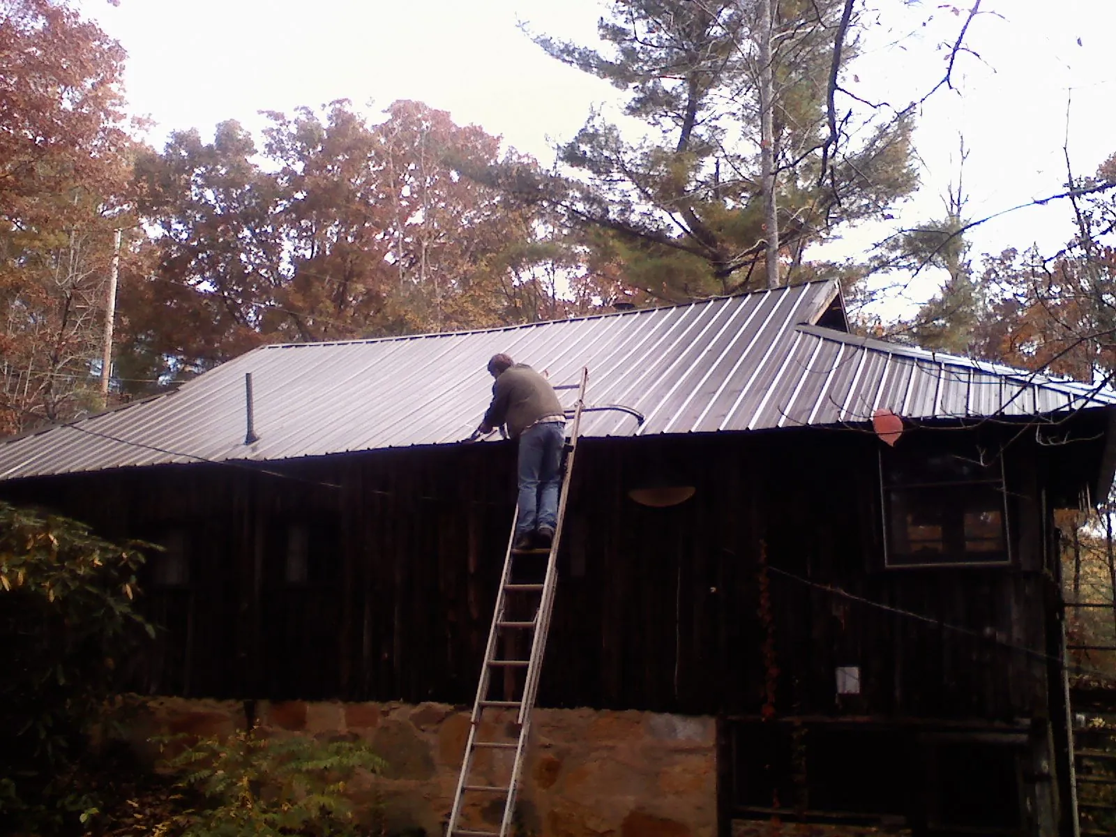 Roofer on a ladder working along the edge of a cabin metal roof in Council