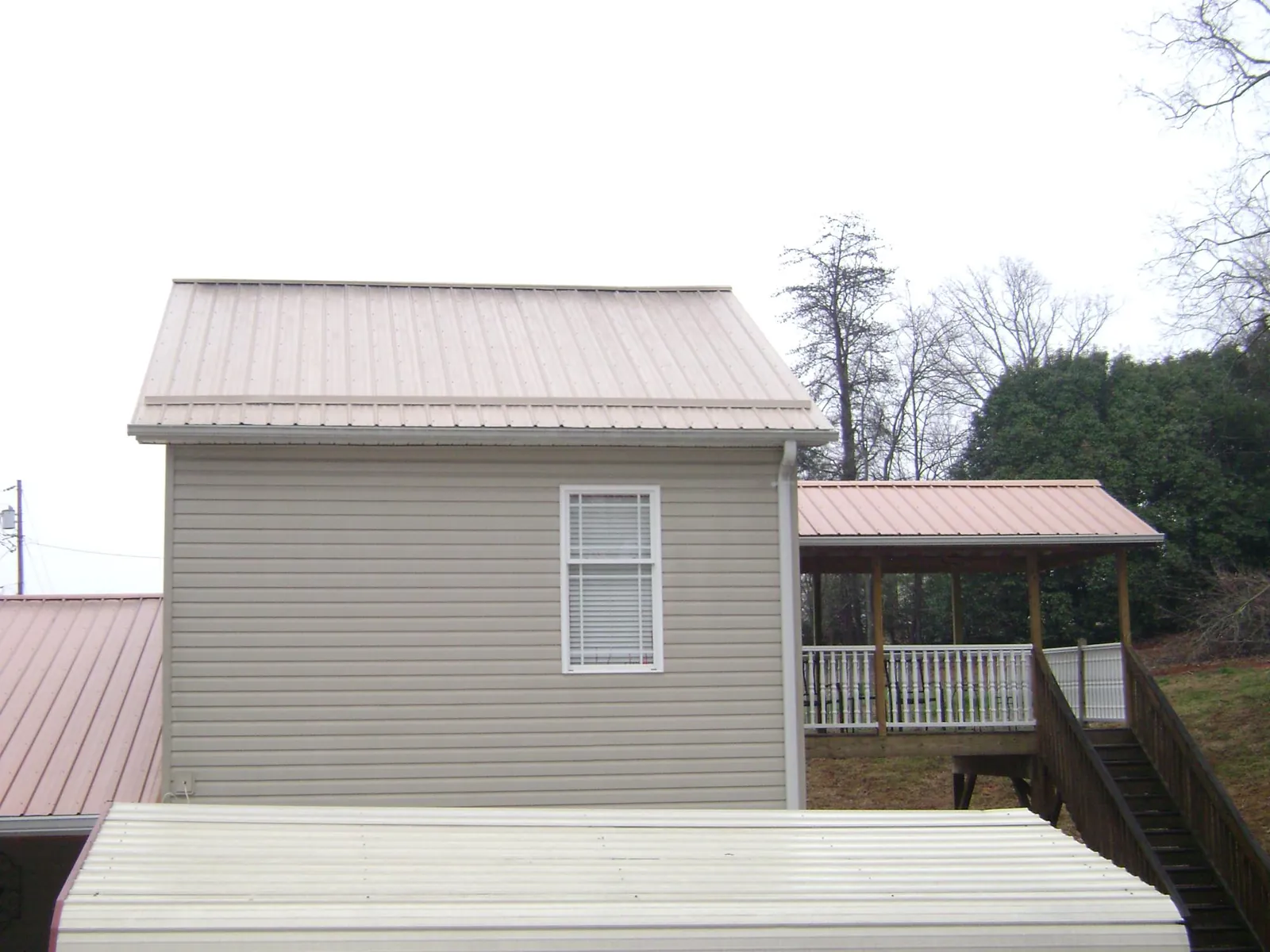 Tan metal roofs on a two story addition and attached porch, from a Roof Replacement job in Council